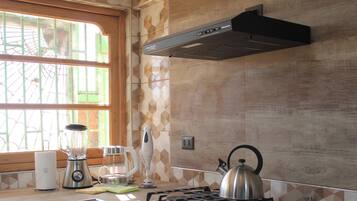 A kitchen with a window, a stove, a kettle, a blender, and a toaster.