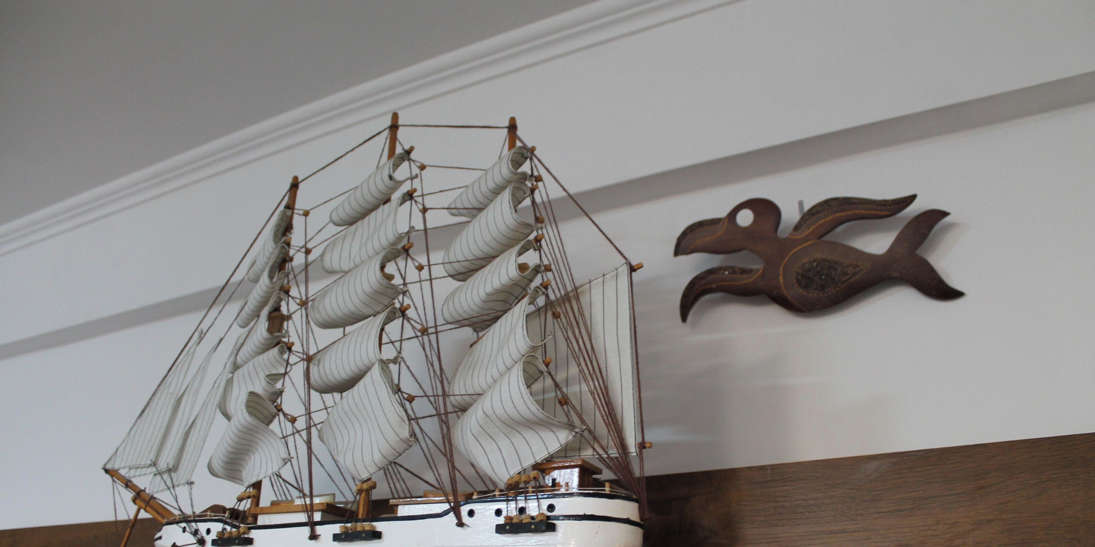 Une maquette de navire avec de nombreuses voiles et une figure de proue en bois, accrochée au mur.