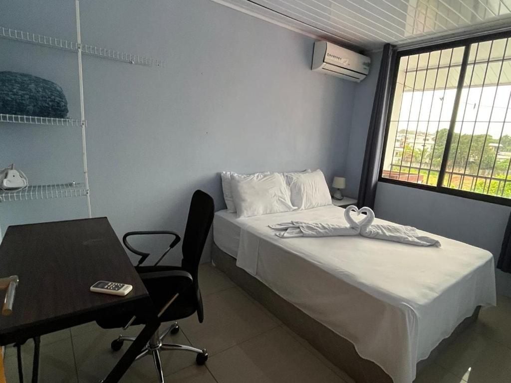 Una cama individual con ropa de cama blanca, un escritorio con silla y una ventana con vista a follaje.