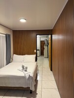 A hotel room with a bed, a wooden panel wall, a tiled floor, and a bathroom visible through an open door.