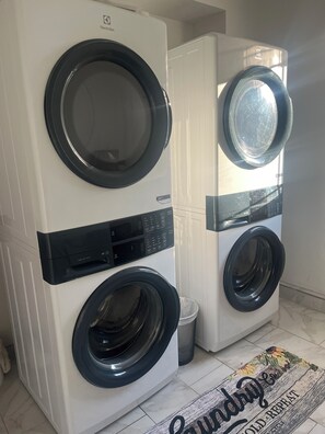Two front-loading washing machines in a laundry room with a tiled floor and a rug with text.
