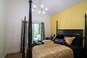 A bedroom with a four-poster bed, a chandelier, and a window with curtains.