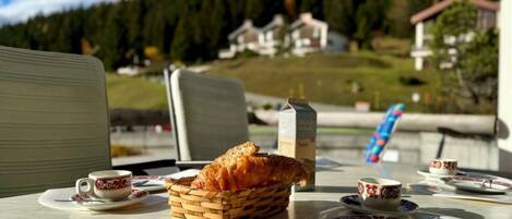 Una mesa servida con una cesta de pan, una botella y platos con tazas, con vistas a un paisaje montañoso.