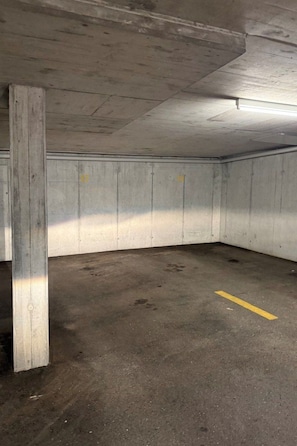An underground parking garage with concrete walls and a yellow line marking on the floor. - Fewoerholungpur (CharmingStay), (Lenzerheide), by Interhome (Lenzerheide)