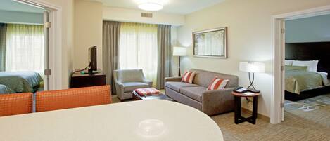 A hotel room with a bed, a sofa, a chair, a desk, and a dining table.