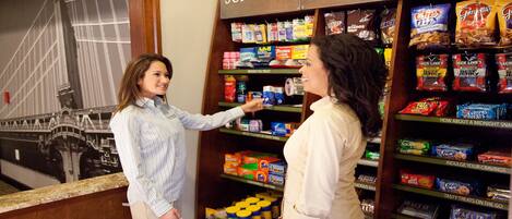 Two people in a store aisle with shelves stocked with various snacks and candies.