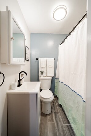 Ein Badezimmer mit weißem Waschbecken, Toilette, Spiegel und Duschvorhang.