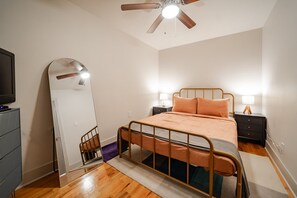 Ein Schlafzimmer mit einem Bett, einem Deckenventilator, einem Spiegel, einer Kommode und einem Nachttisch mit Lampe.