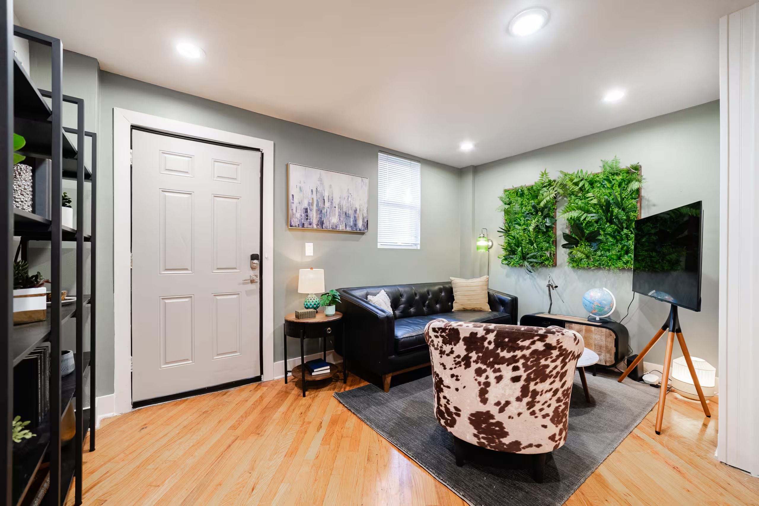 A modern living room with a black leather sofa, a unique patterned armchair, a flat-screen TV, and a green wall feature.