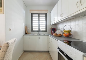 A compact kitchen with white cabinets, a window, and a stove. - Elegant Apt 50meters Close Acropolis (Athina)