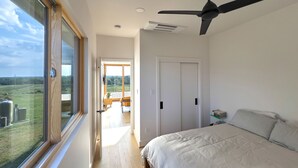 A bedroom with a bed, a ceiling fan, a view through a large window, and a door leading to a balcony. - Luxe Farmhouse with Scenic Views and Cowboy Pool (Fayetteville)