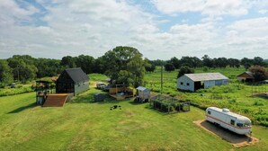 Una propietat rural amb una granja, una zona d'estar exterior coberta i una caravana.