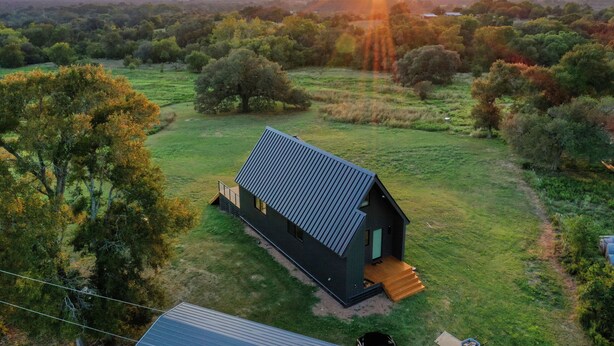 A modern house with a sloped roof, surrounded by a grassy field and trees. - Luxe Farmhouse with Scenic Views and Cowboy Pool (Fayetteville)