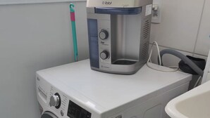 A compact, modern laundry room with a front-loading washing machine and a stacked dryer. - Pearl Apartment (Sumaré)