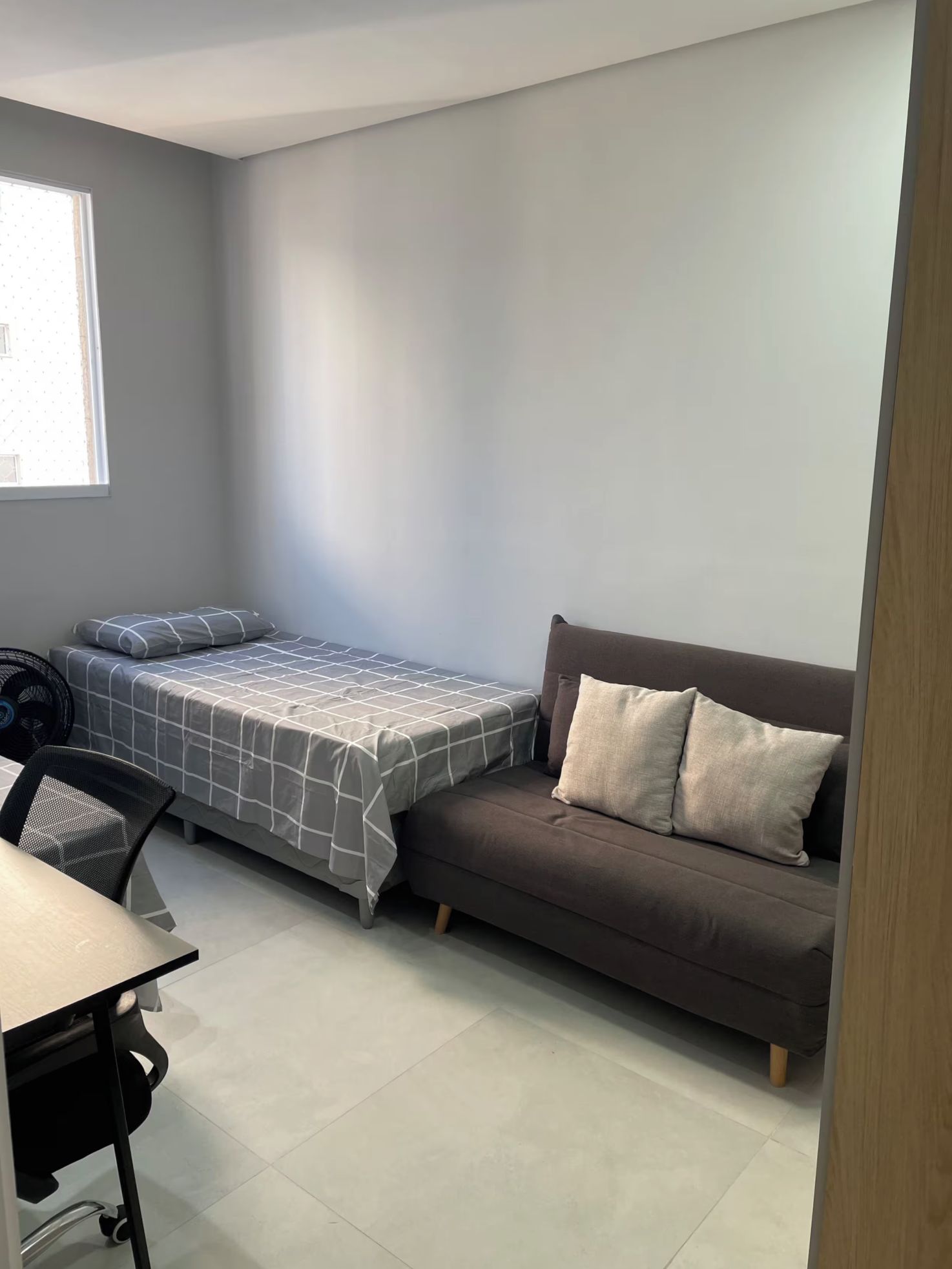 Una habitación pequeña y moderna con una cama, un sofá y un escritorio con una silla.