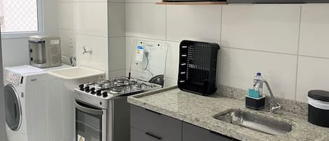 Une cuisine moderne avec des meubles gris, un four à micro-ondes encastré, une cuisinière à gaz et une machine à café.
