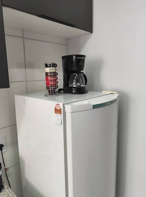 Un réfrigérateur blanc, avec une machine à café posée sur le dessus, un calendrier et un récipient doté d’étiquettes.