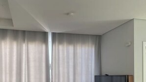 A room with a large window, a flat-screen TV, and a ceiling light. - Pearl Apartment (Sumaré)