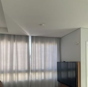 Une pièce dotée d’une grande fenêtre, d’un téléviseur à écran plat et d’un luminaire au plafond.
