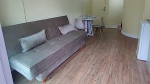 A small living area with a sofa, a dining table with chairs, and a refrigerator. - Apartamento Cristal Feirinha Liberade SP (São Paulo)