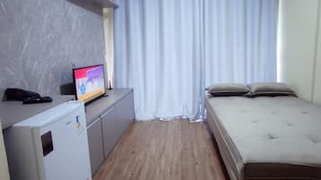Une petite pièce, de taille modeste, comprenant un lit, un bureau avec un ordinateur et une fenêtre avec des rideaux.