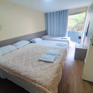 Habitación de hotel con dos camas, una ventana con cortinas y vista a árboles.