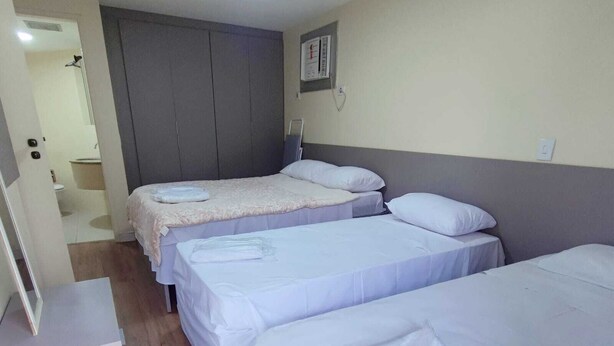 A hotel room with three single beds, a wardrobe, and a bathroom visible through an open door. - Apartamento Cristal Feirinha Liberade SP (São Paulo)
