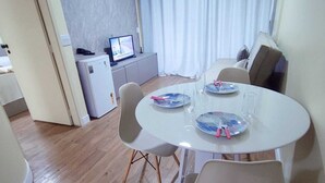 A dining area with a round table, white chairs, and a small kitchen in the background. - Apartamento Cristal Feirinha Liberade SP (São Paulo)