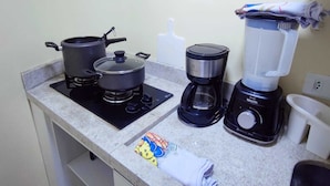 A kitchen with a stove, a coffee maker, and a blender on the countertop. - Apartamento Cristal Feirinha Liberade SP (São Paulo)