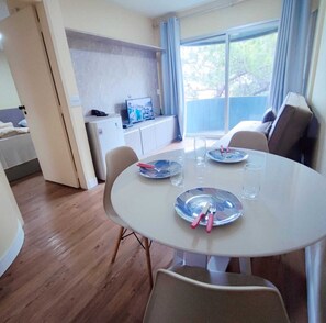 A dining area with a round table, chairs, and a television in the background. - Apartamento Cristal Feirinha Liberade SP (São Paulo)