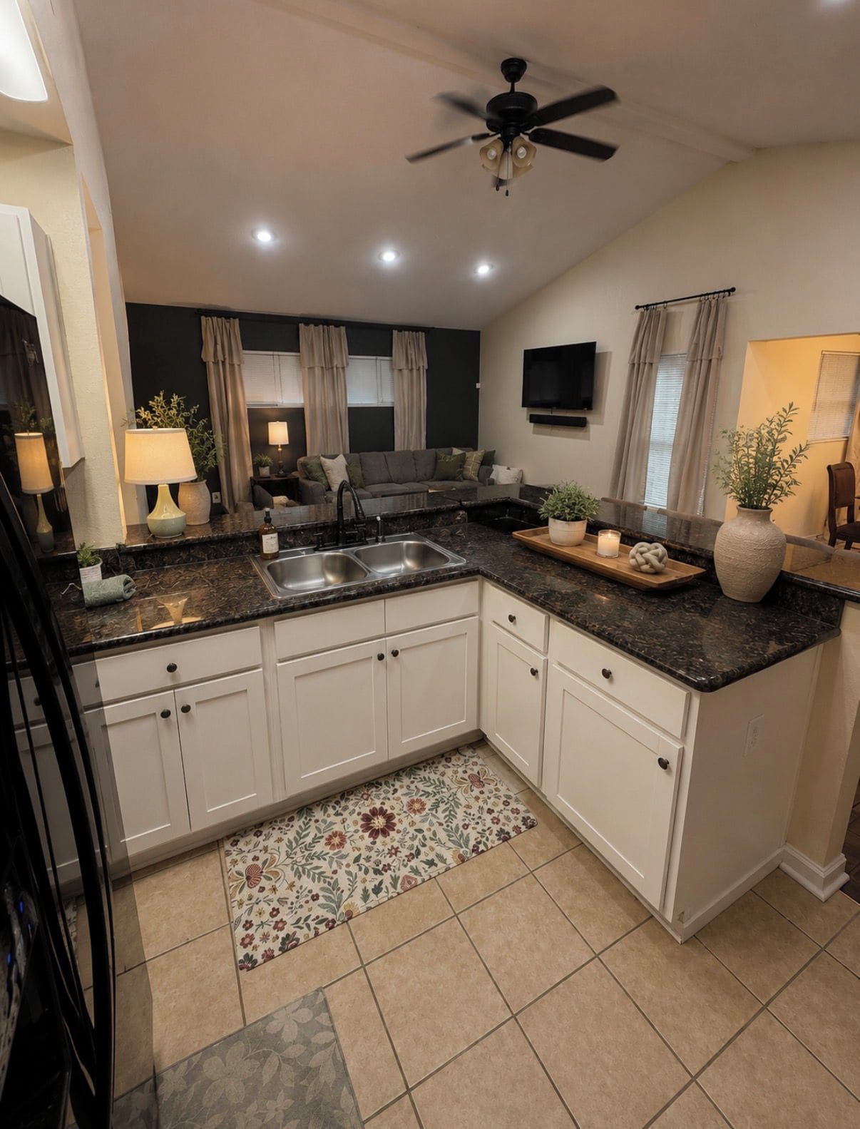A modern kitchen with white cabinets, a black countertop, and a ceiling fan.