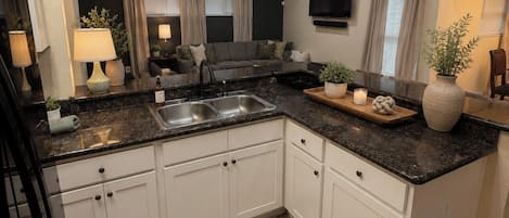 A modern kitchen with white cabinets, a black countertop, and a ceiling fan.