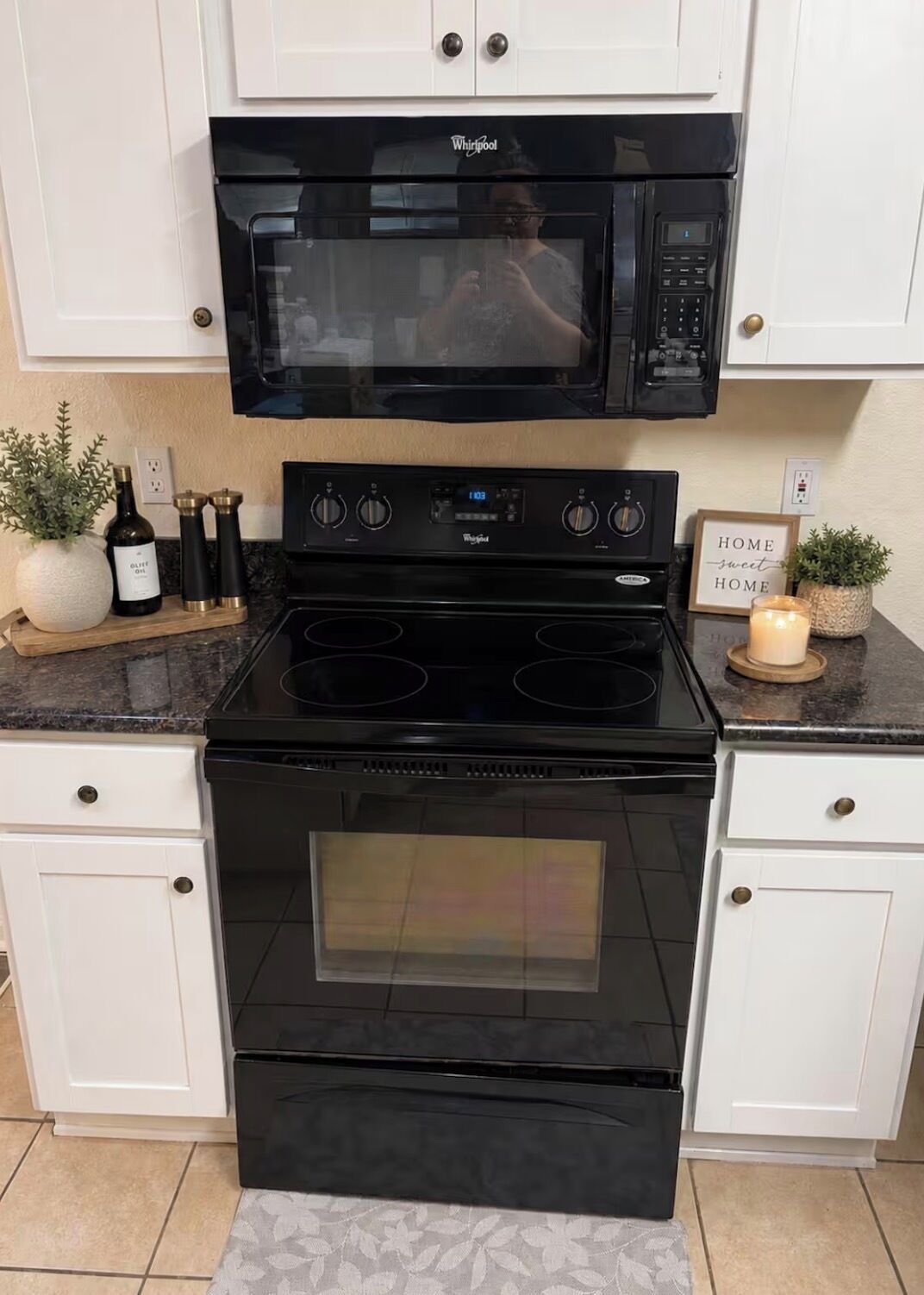 A kitchen with a black Whirlpool stove, microwave, and oven, white cabinetry, and a small potted plant on the countertop.