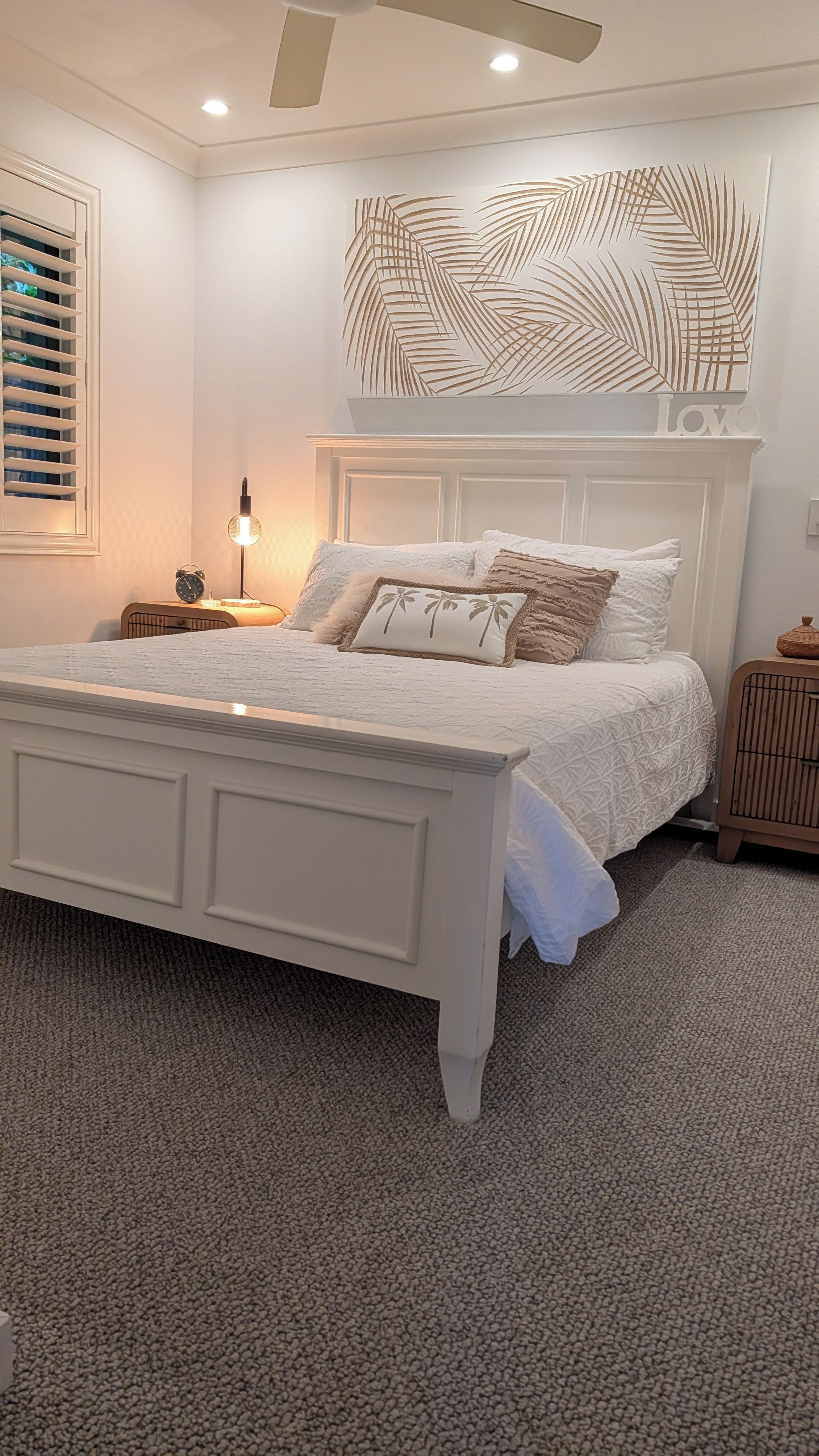 Une chambre à coucher comprenant un lit, une table de chevet, une lampe, un élément décoratif mural et un ventilateur de plafond.
