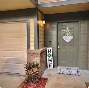 A residential house with a garage door, a brick pillar, a welcome sign, and a door with a number plate. - Tally Townhome Minutes from FAMU & FSU (Tallahassee)