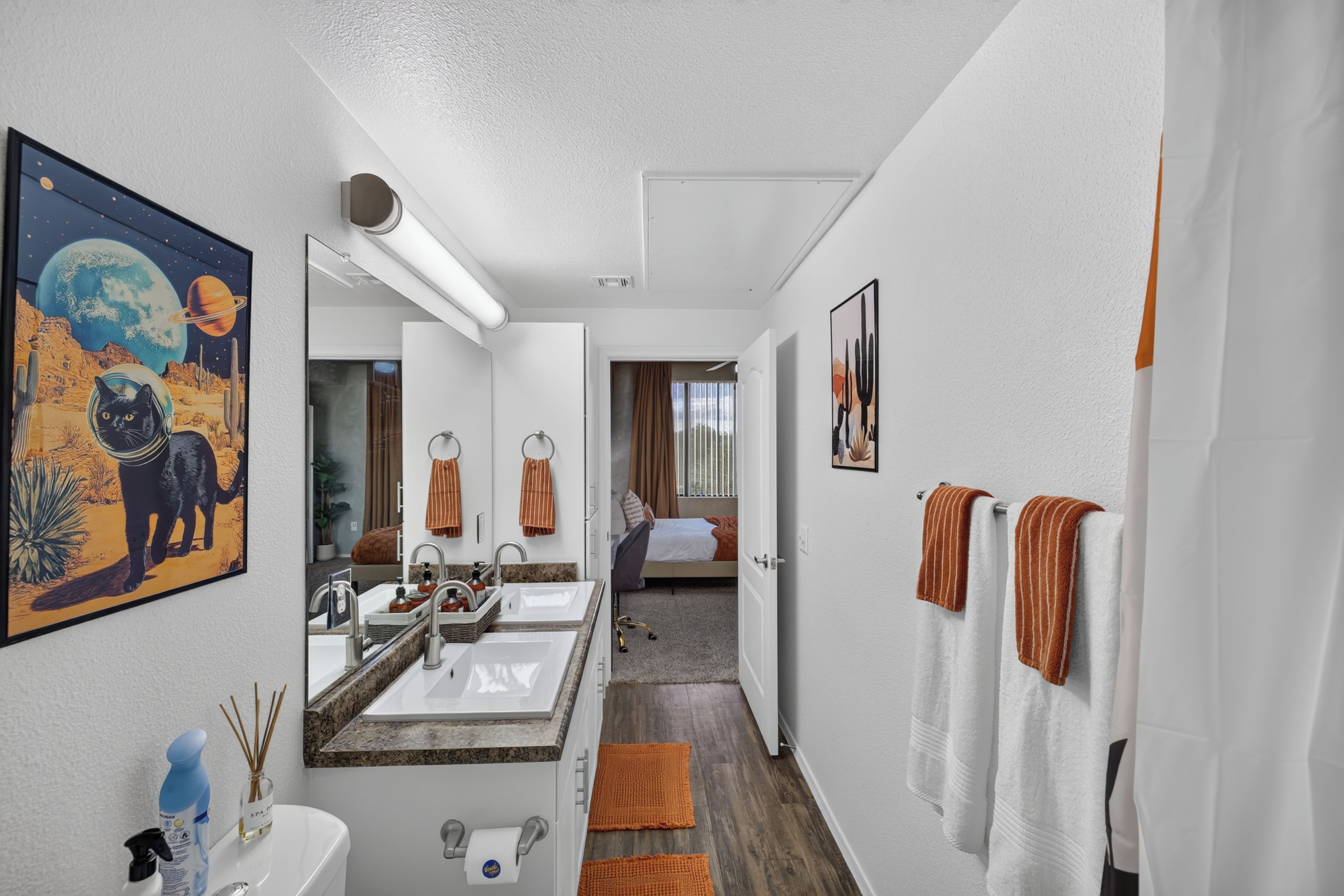 A hotel bathroom with dual sinks, a large mirror, and a painting of a cat in a space suit.