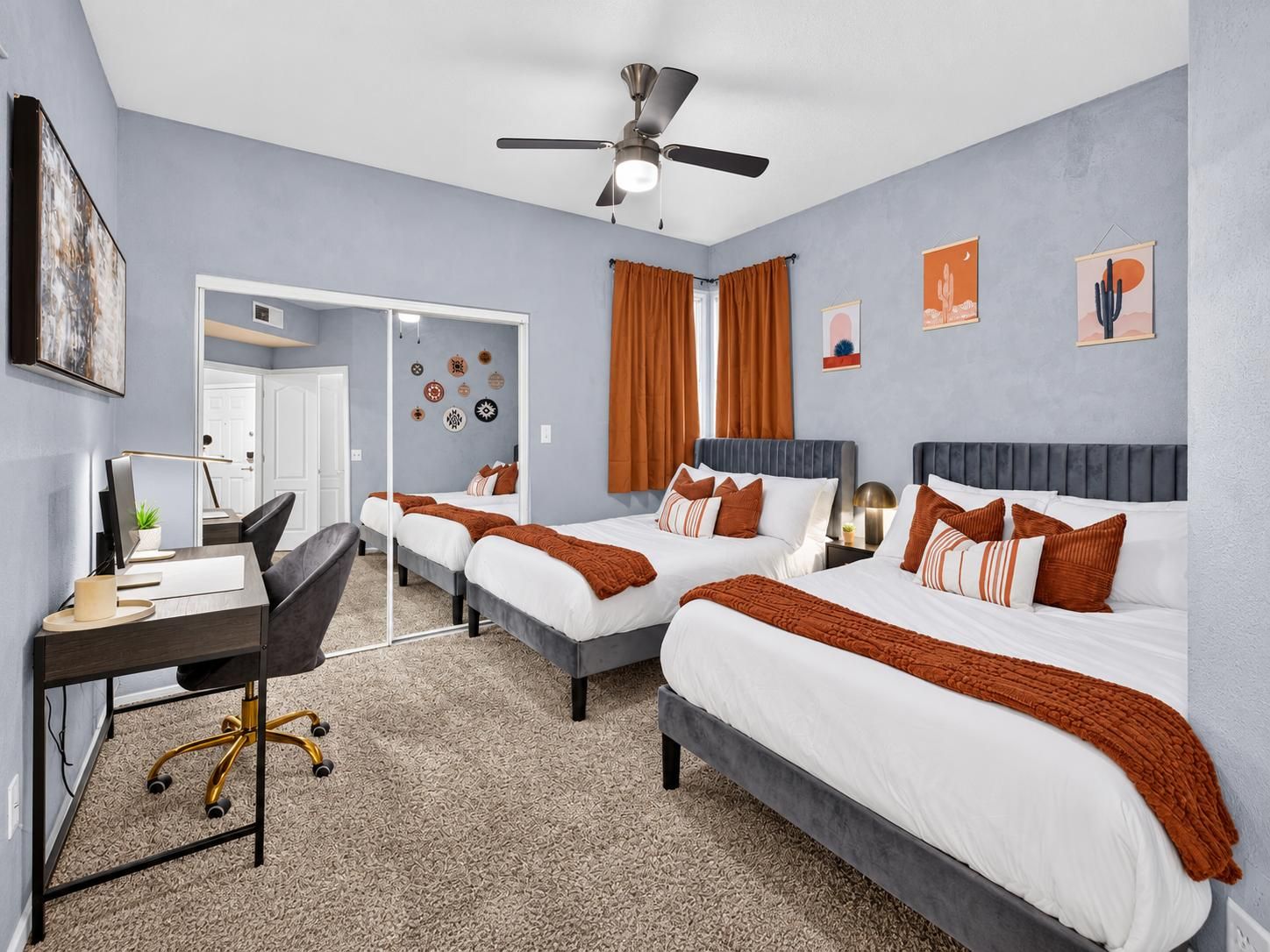 Une chambre d’hôtel avec deux lits, un bureau, une chaise et un ventilateur de plafond.