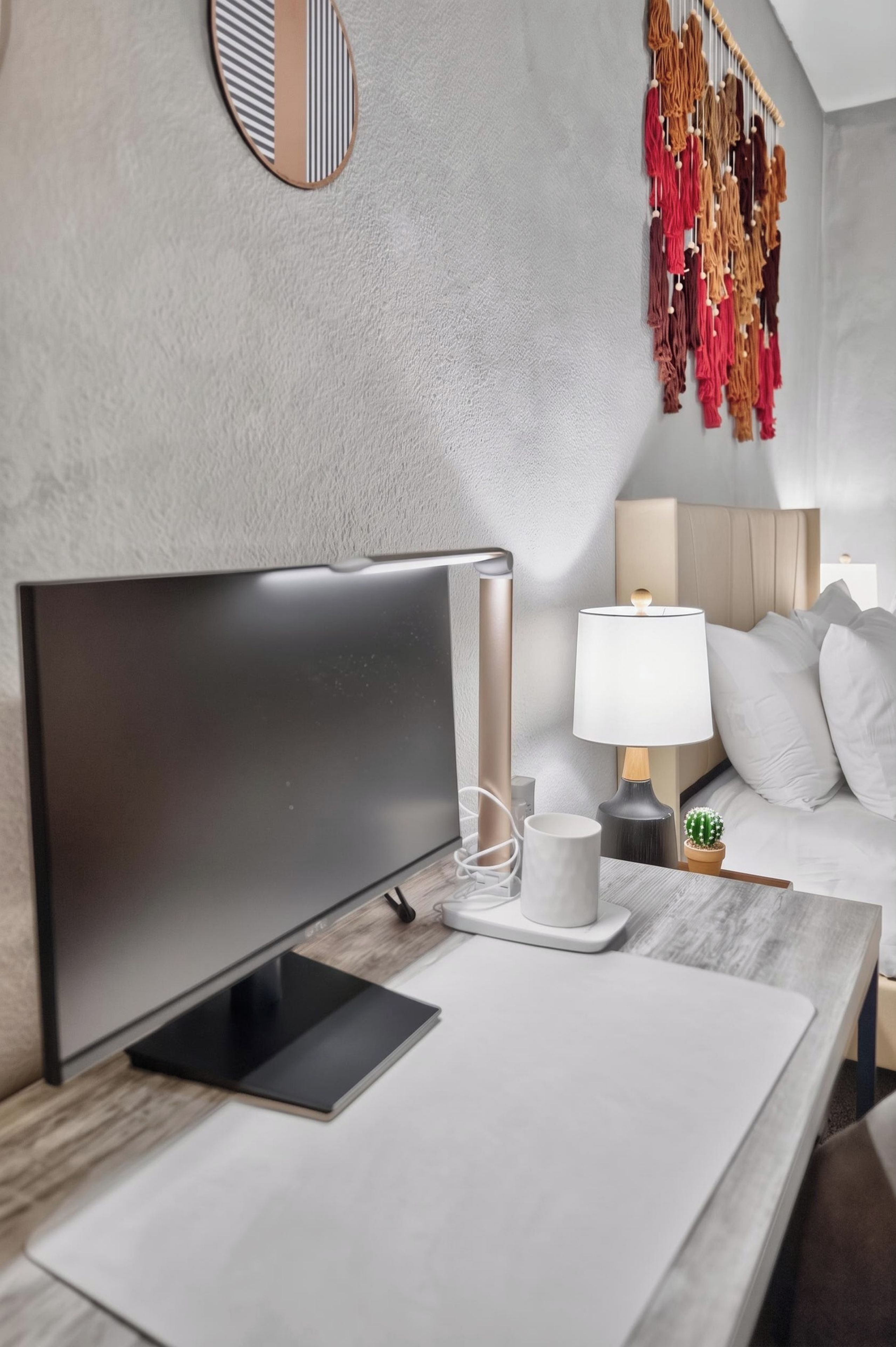 A modern hotel room with a bed, bedside table, lamp, and a wall-mounted decorative item.