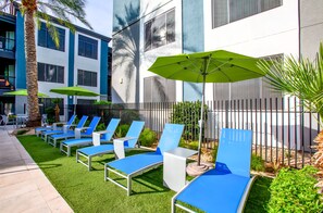 A poolside area with lounge chairs and umbrellas, a palm tree, and a building with large windows. - Tranquil Escape Pool-Gym-Free Parking 1st Floor (Phoenix)