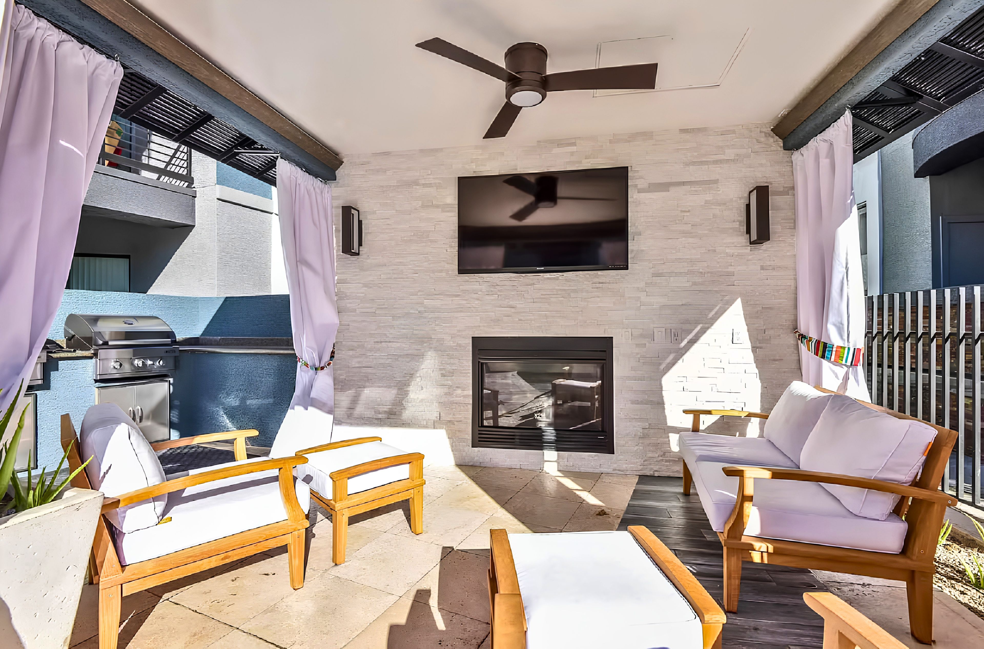 An outdoor patio with a ceiling fan, a flat-screen TV, and a fireplace.
