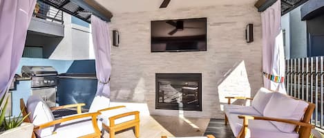 An outdoor patio with a ceiling fan, a flat-screen TV, and a fireplace.