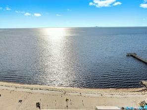 Ein Strand mit einem Steg, der sich ins Wasser erstreckt, bewölkter Himmel und eine entfernte Skyline.