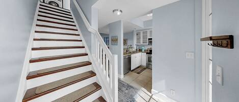 A staircase with wooden steps and a handrail, leading to a kitchen area with white cabinets and a window.