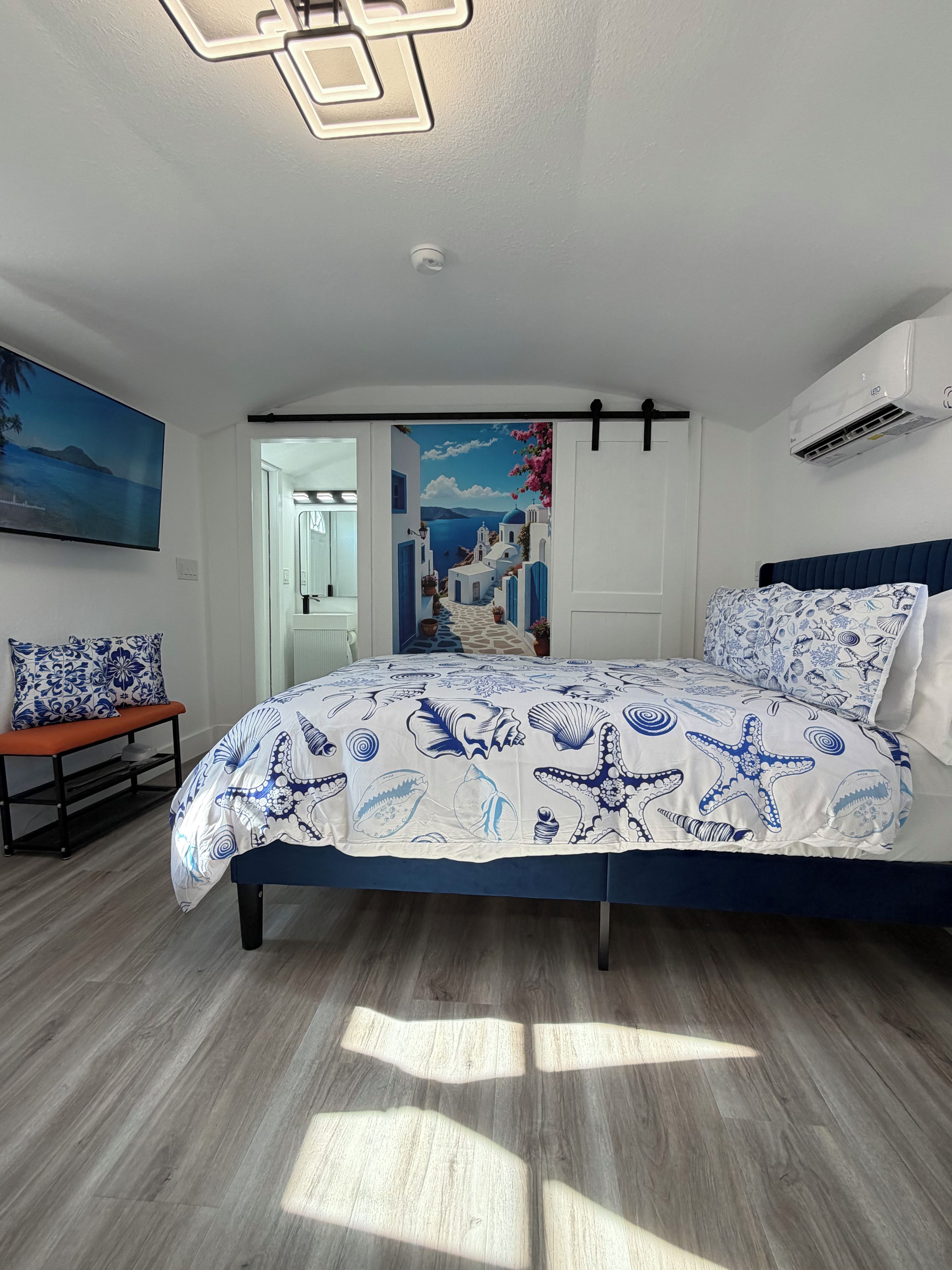 Une chambre à coucher comprenant un lit, un banc, un climatiseur fixé au mur et une porte donnant sur une autre pièce.