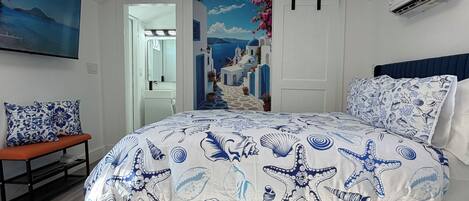 Une chambre à coucher comprenant un lit, un banc, un climatiseur fixé au mur et une porte donnant sur une autre pièce.