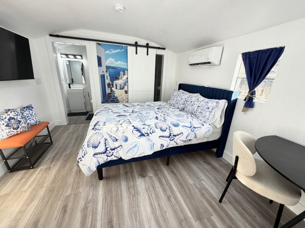 Une chambre à coucher comprenant un lit, un banc, un bureau et un climatiseur fixé au mur.