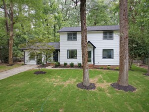 A two-story house with a front yard, surrounded by trees.