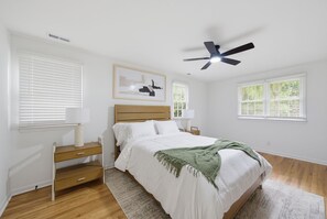 A bedroom with a bed, bedside tables, a ceiling fan, and windows with blinds.