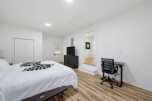 Een slaapkamer met een bed, een dressoir, een bureau met stoel en een spiegel.