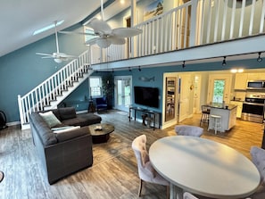 A spacious living area with a grey sofa, a round dining table, and a staircase leading to an upper level. - Stylish home w all the comforts in a bay front community near beaches & shopping (Lewes)